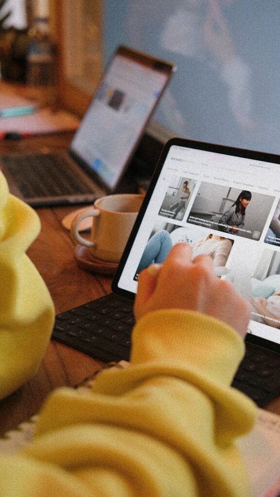Close-up of a hand using a tablet in a cozy workspace environment with a laptop nearby.